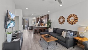 A modern living room with a sofa, coffee table, and TV. There is a kitchen in the background with a dining area. - The Lofts 2|Community Pool w/water slide and hot tub, grill, Smart TV (Saint George)