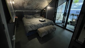 Une chambre moderne avec un grand lit, un banc et une porte-fenêtre coulissante donnant sur un balcon.