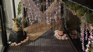 Un hamac suspendu entre deux murs, agrémenté de guirlandes lumineuses et entouré de plantes en pot et de pierres décoratives.