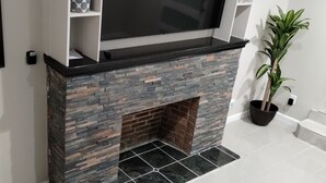 A modern fireplace with a stone facade, a flat-screen TV mounted above it, and a potted plant to the right. - Best Choice. Spacious, 1BR 1BA Apt in NW DC area with free street parking. (Washington)