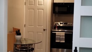 A modern kitchen with stainless steel appliances, a dining area with a glass table and metal chairs, and a white door with a frosted glass panel. - Best Choice. Spacious, 1BR 1BA Apt in NW DC area with free street parking. (Washington)