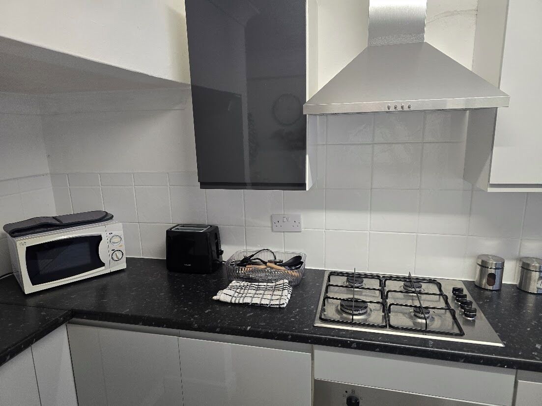 A kitchen with a microwave, toaster, gas stove, and a hanging pot rack.