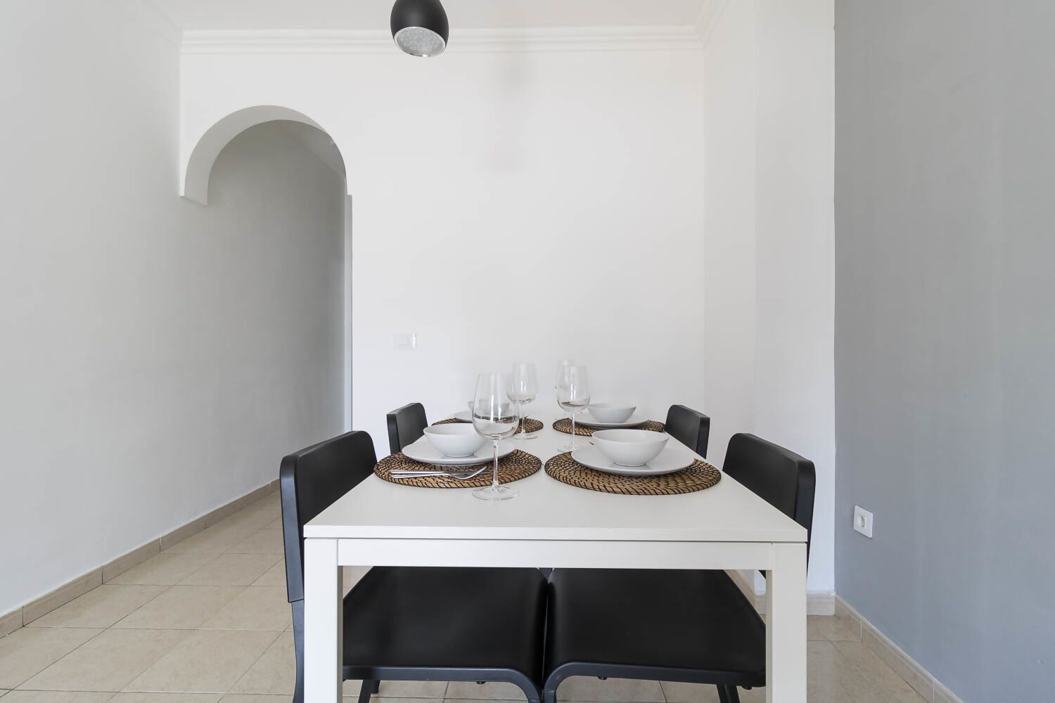 Een eethoek met een witte tafel voor vier personen, zwarte stoelen en een moderne hanglamp.