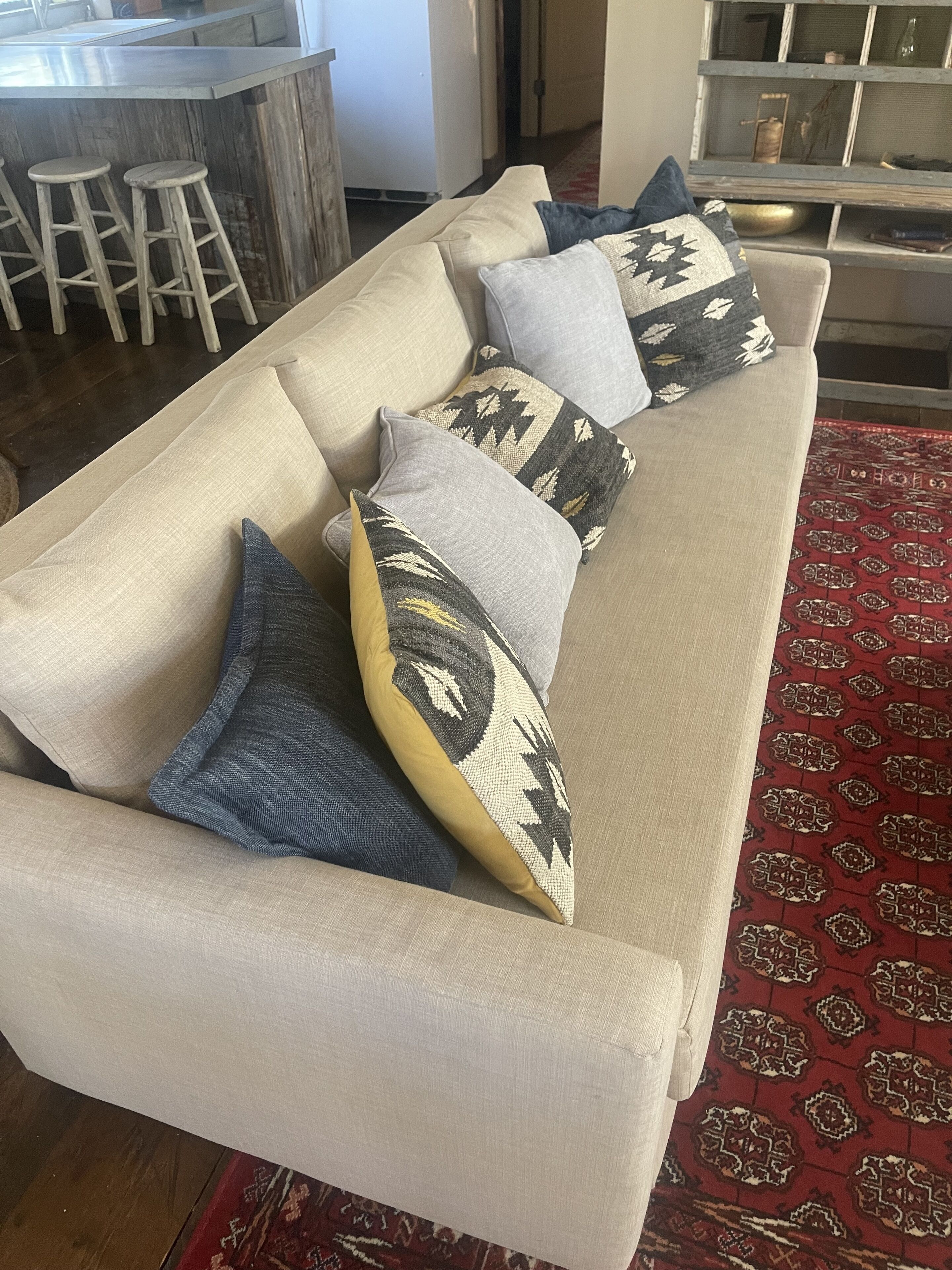 A beige sofa with patterned cushions, a wooden bar area, and a patterned rug.