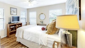 Un dormitorio con cama, televisión, estantería, lámpara y ventana.