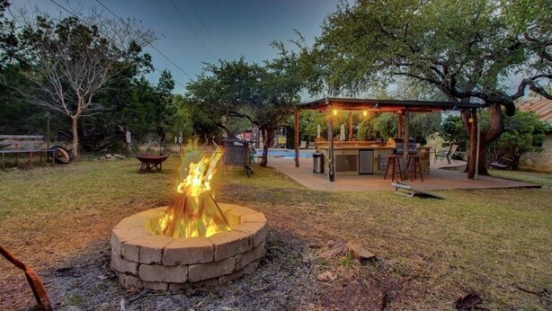 Un patio trasero con un pozo de fuego, una pérgola de madera y una zona de barbacoa.