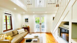 Un vaste salon doté d’un haut plafond, d’un escalier et offrant une vue sur l’extérieur.
