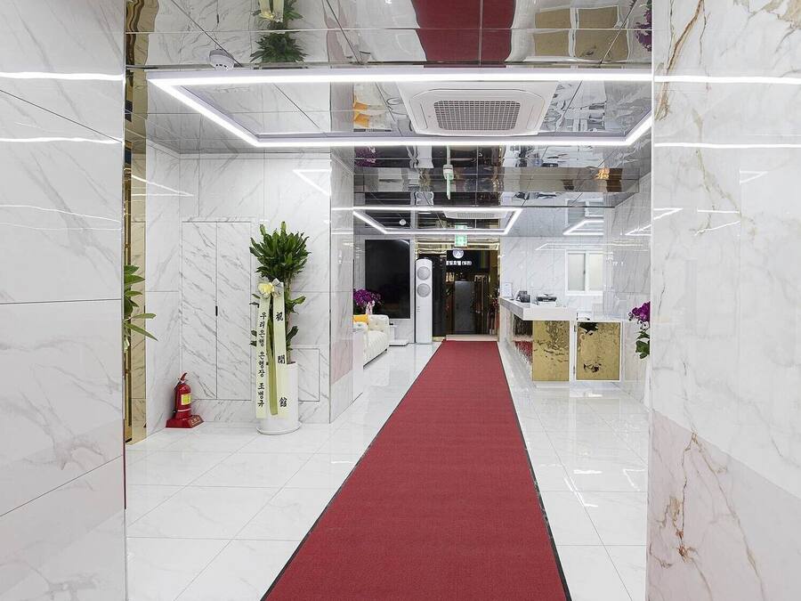 A hotel lobby with a marble floor, a red carpet, and a reception desk.