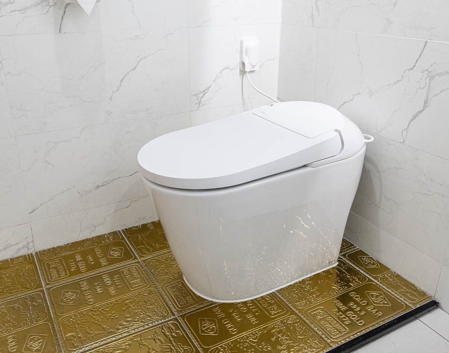 A white toilet in a bathroom with marble walls and gold-patterned floor tiles.