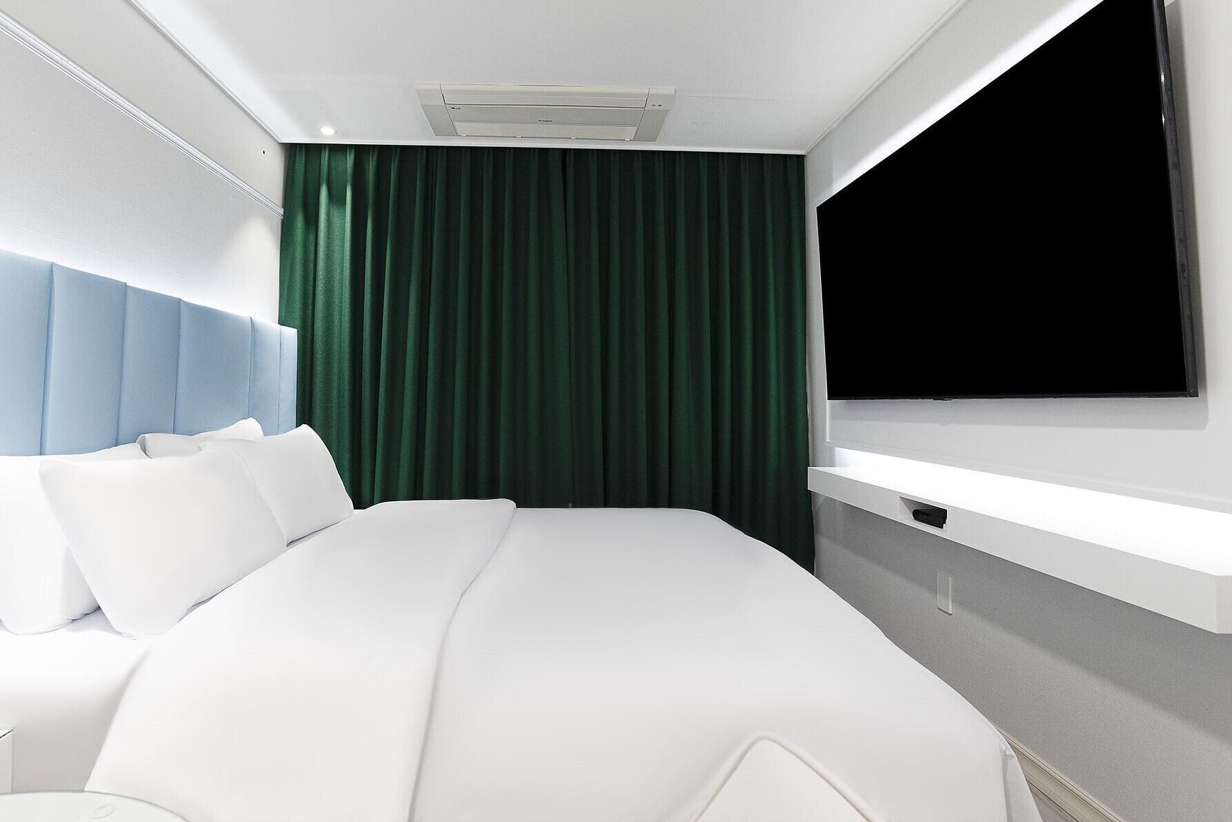 Een moderne hotelkamer met een groot bed, een hoofdbord, een flatscreen televisie aan de muur en een raam met gordijnen.
