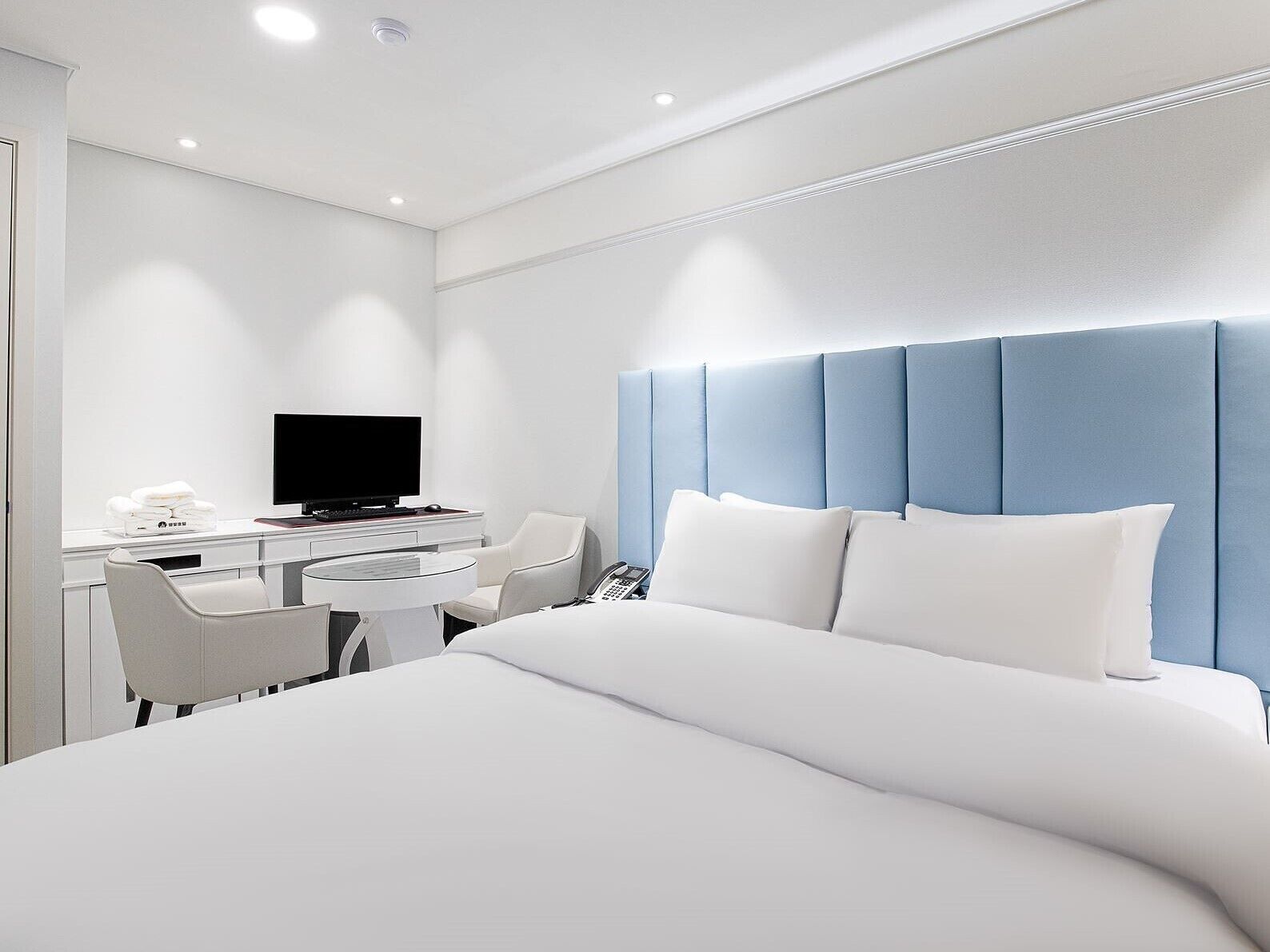 Quarto de hotel moderno com uma cama grande, uma escrivaninha com televisão de tela plana e uma cadeira.