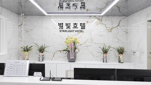 A reception desk with a marble wall background, a sign reading "STARLIGHT HOTEL", and several potted plants. - Star Light (Seoul)
