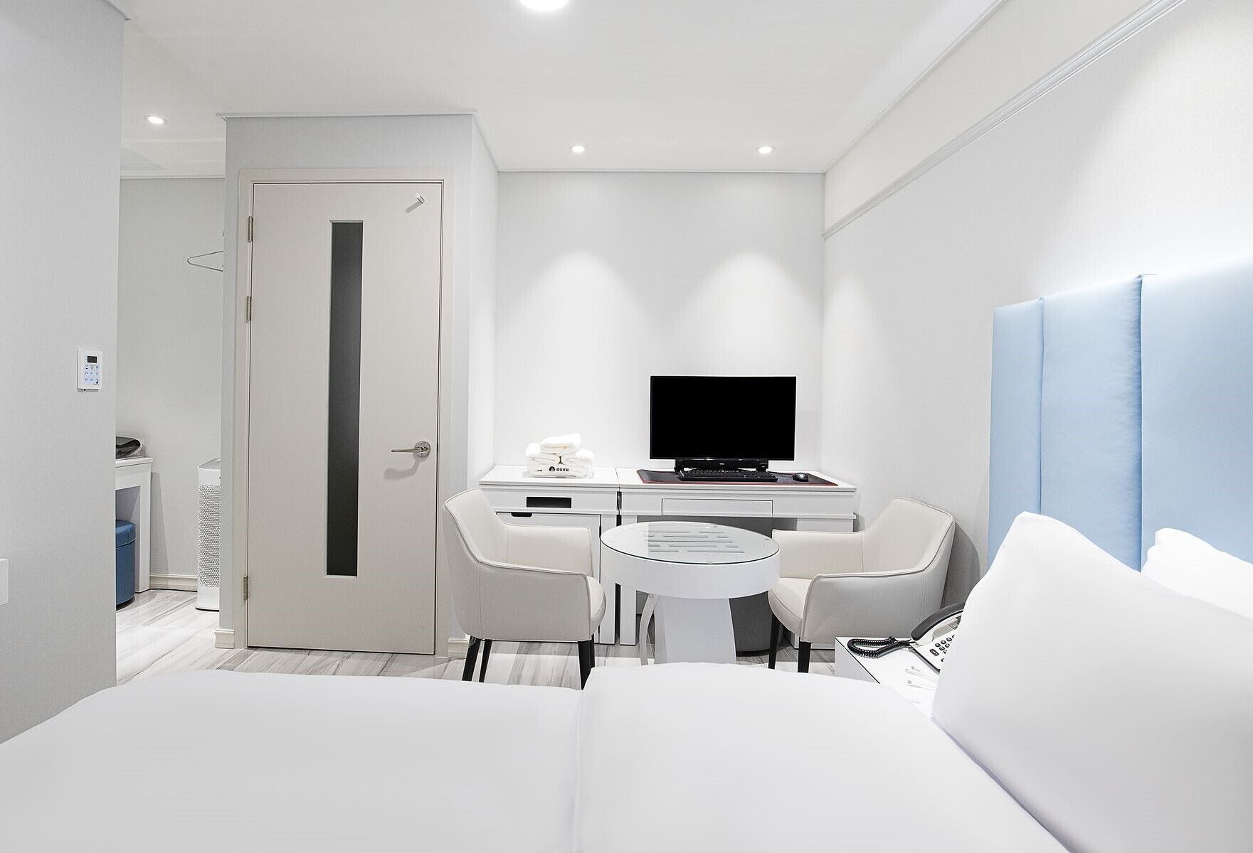 A modern hotel room with a bed, a desk with a computer, a TV, and a seating area.