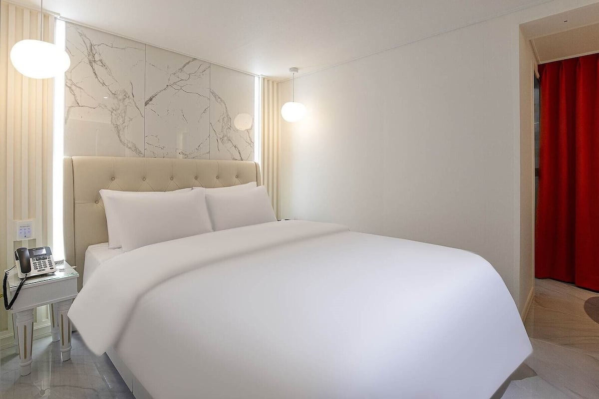A hotel room with a large bed, a marble wall, a telephone, and a red curtain.