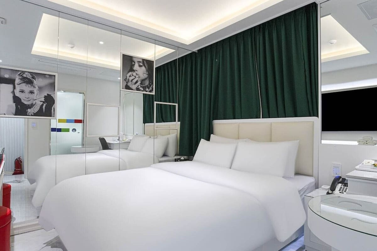 A modern hotel room with two beds, a large mirror, and a vanity with a phone.
