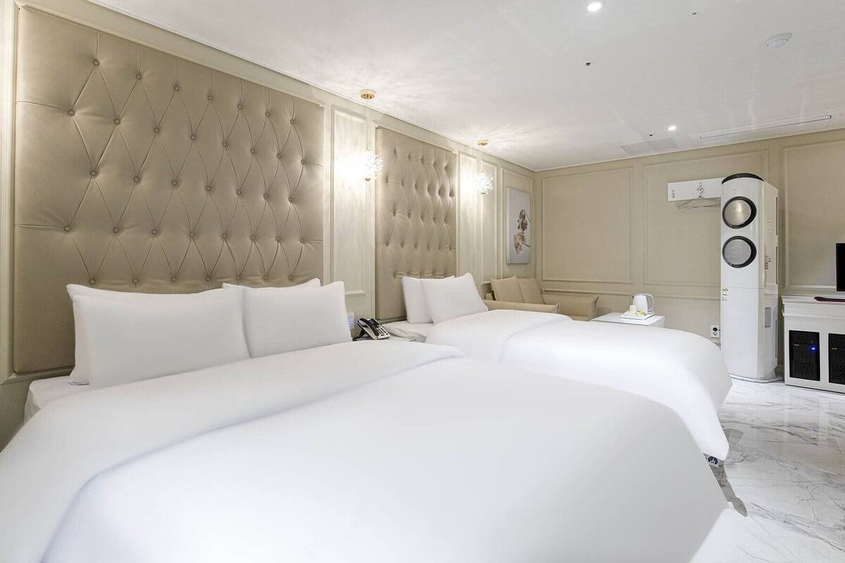 A hotel room with two large beds, a minibar, and a ceiling-mounted air conditioning unit.