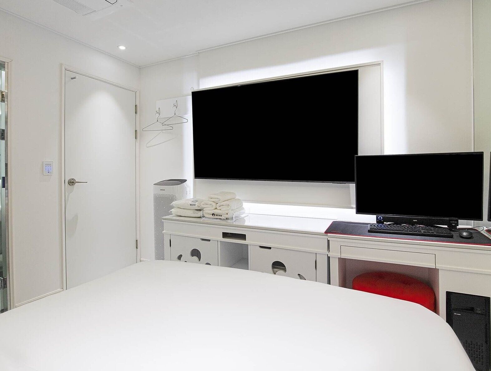 Una habitación de hotel con cama, escritorio, computadora, televisor y armario.