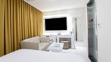 A hotel room with a bed, a sofa, a TV, a desk, a mirror, and an elevator.