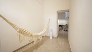 A hallway with a hammock, a white vase, and a kitchen in the background. - GuestHost - La Mille - Charming Ostuni Apartment (Ostuni)