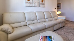 A beige sofa in a room with a tiled floor, a framed abstract painting, and a lamp. - GuestHost - Alghero Sea View Apartment with Balcony! (Alghero)