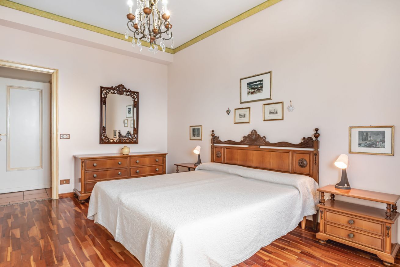 Een slaapkamer met een houten bed, een dressoir, een nachtkastje, een spiegel en lijstjes met foto's aan de muur.