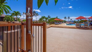 Una valla de madera con un área de piscina al fondo, que incluye sombrillas rojas y sillones de descanso.