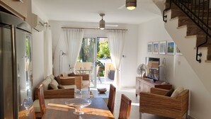 A spacious living area with a wooden dining table, wicker sofas, and a television.