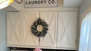 A laundry room with two washing machines, a dryer, a sign above the machines, and a wreath on the wall.