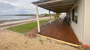 Ein überdachter Außenbereich mit Holzterrasse, einer Sitzecke mit Stühlen und Blick auf Strand und Meer.
