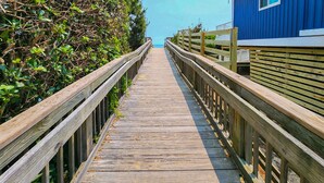 A wooden boardwalk leading to a blue building with a wooden railing on both sides.