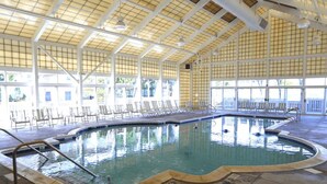 An indoor swimming pool with a tiled floor, surrounded by lounge chairs and a high ceiling with a grid pattern.