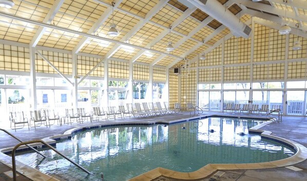 An indoor swimming pool with a tiled floor, surrounded by lounge chairs and a high ceiling with a grid pattern.
