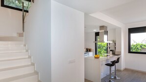 A modern kitchen with a central island, a staircase, and a large window.