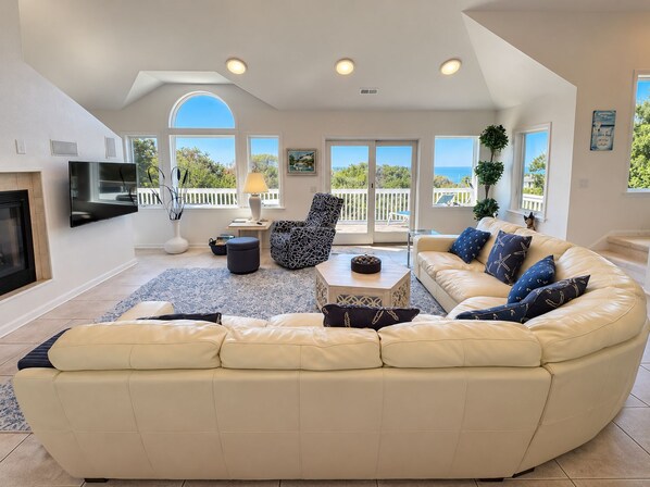 A modern living room with a curved sofa, a flat-screen TV, and large windows offering a view of the outdoors.