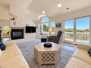 A spacious living room with a fireplace, a television, and a balcony with a view.