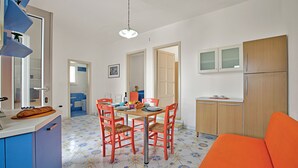 Eine kleine Küche mit Essbereich, ausgestattet mit einem Holztisch, roten Stühlen und einem blau-gelb gemusterten Boden.