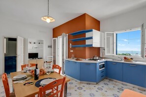 Una cocina moderna con armarios azules, una zona de comedor con sillas anaranjadas y un ventanal con vistas.