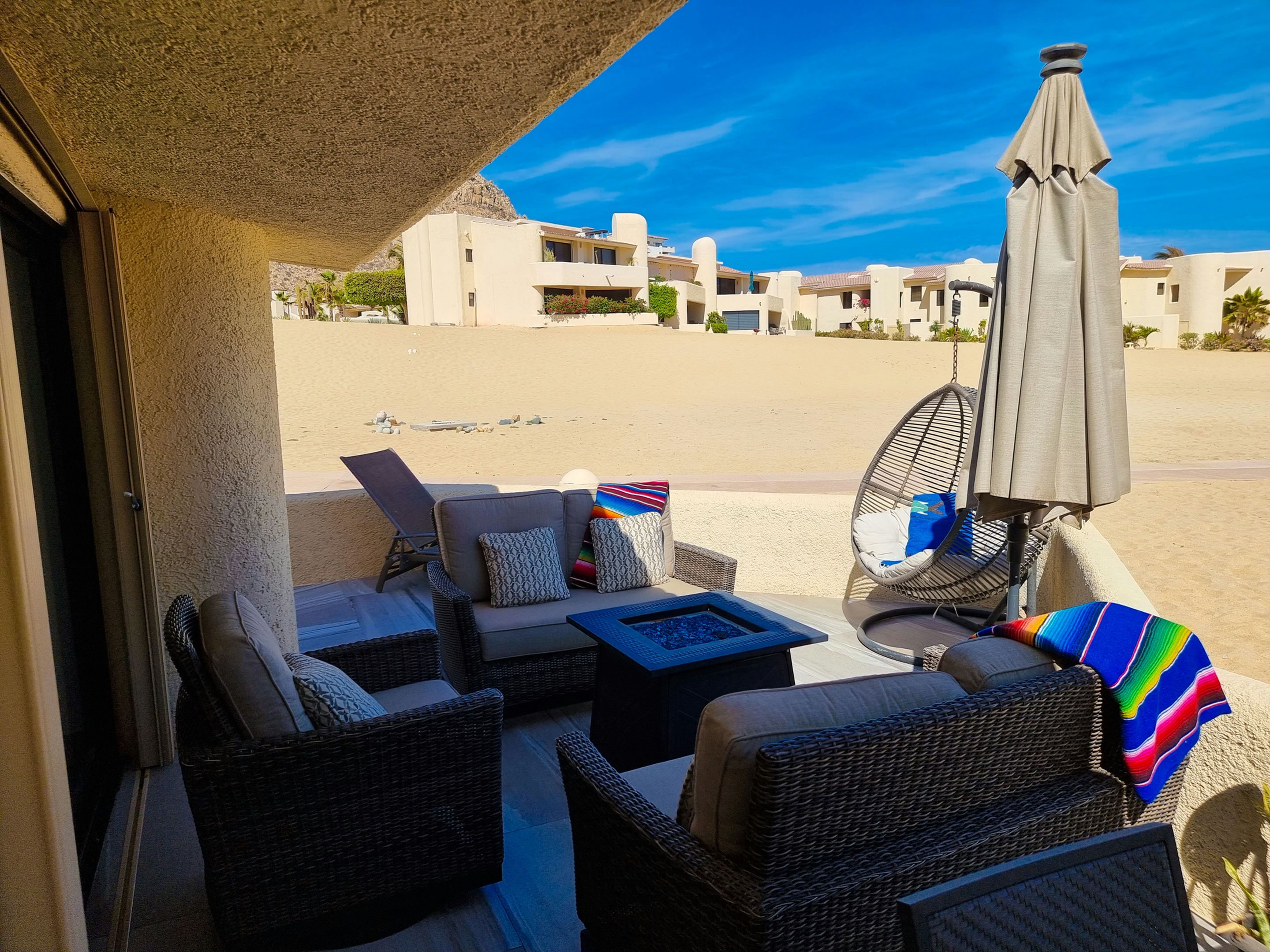 A sunlit outdoor seating area with wicker furniture, a table, and a beach view.