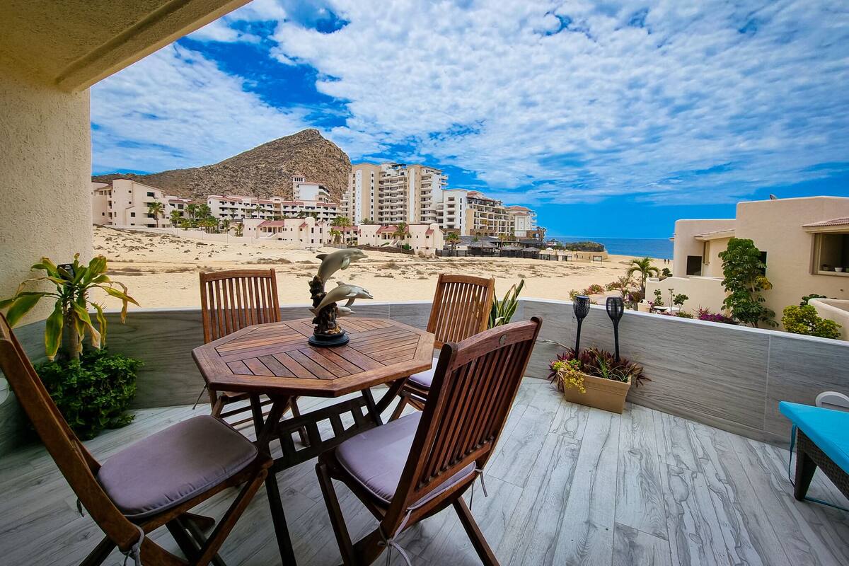 Una mesa y sillas de madera en un balcón con vistas a una playa y edificios de un hotel.
