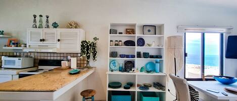 A kitchen with a central island, stools, a microwave, and a shelf with various kitchenware.