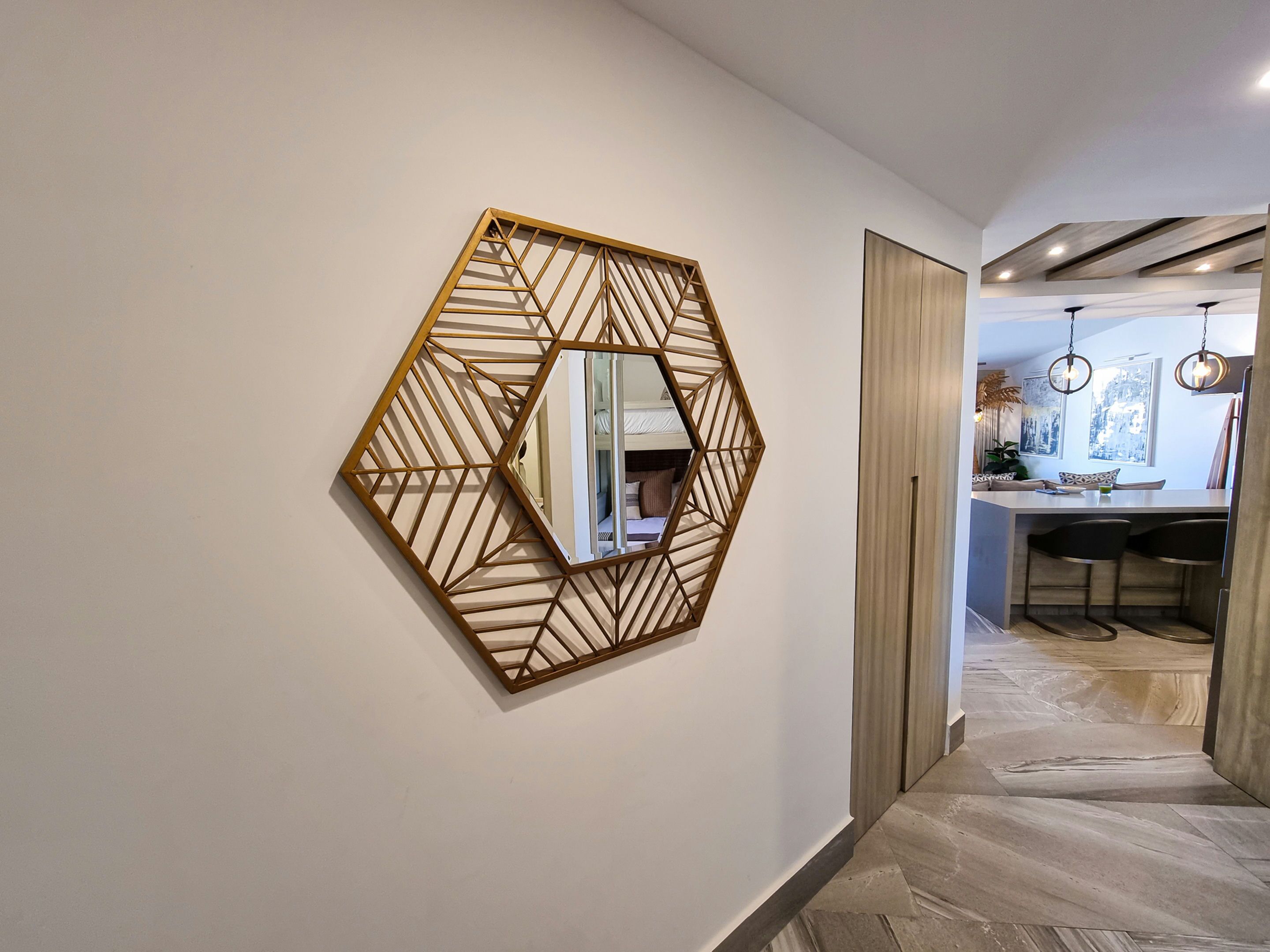 A hallway with a geometric wall art piece, a kitchen area with bar stools, and a dining table.