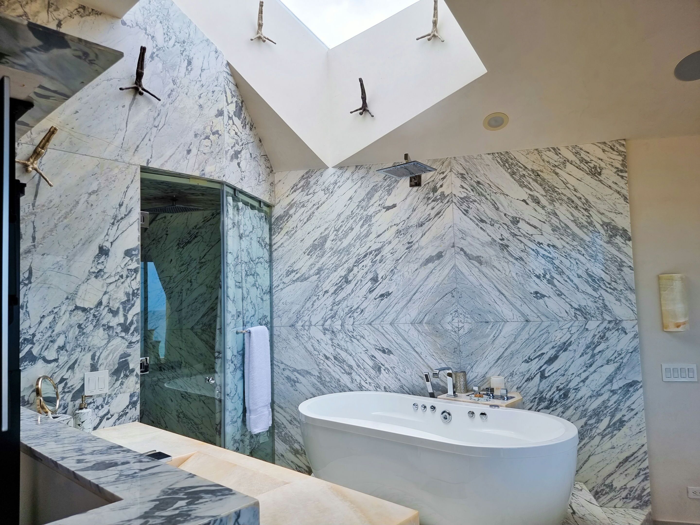 A modern bathroom with a freestanding bathtub, marble walls, and a glass shower enclosure.