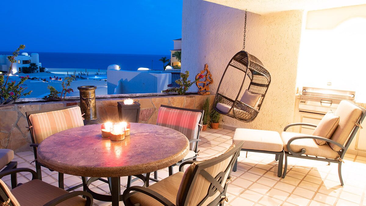 Una mesa redonda con sillas y un sillón colgante en un balcón con vista al mar.
