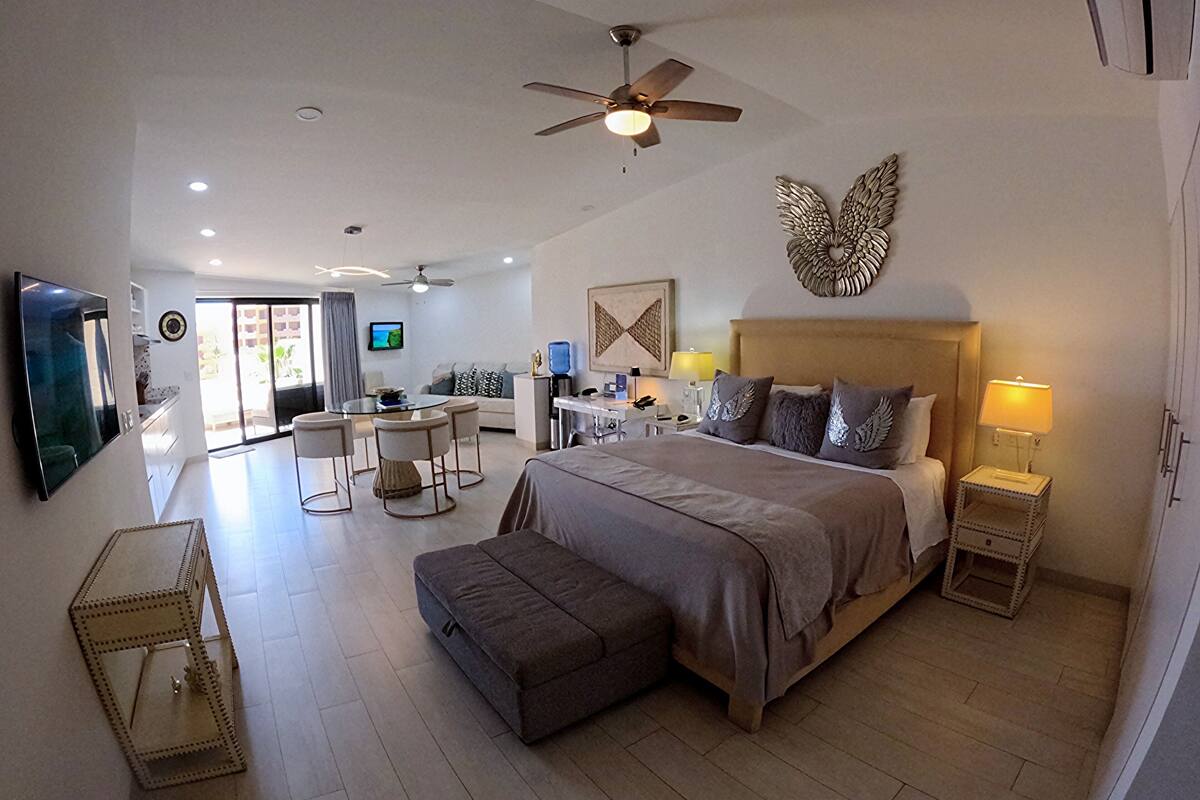 Un dormitorio amplio con una cama grande, un ventilador de techo y un televisor montado en la pared.