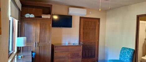 A room with a ceiling fan, a flat-screen TV, wooden wardrobes, a desk with a lamp, and a patterned chair.