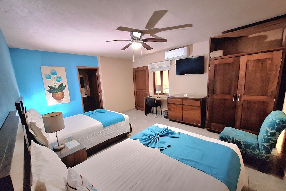 A hotel room with two beds, a ceiling fan, a TV, a desk, and a wardrobe.