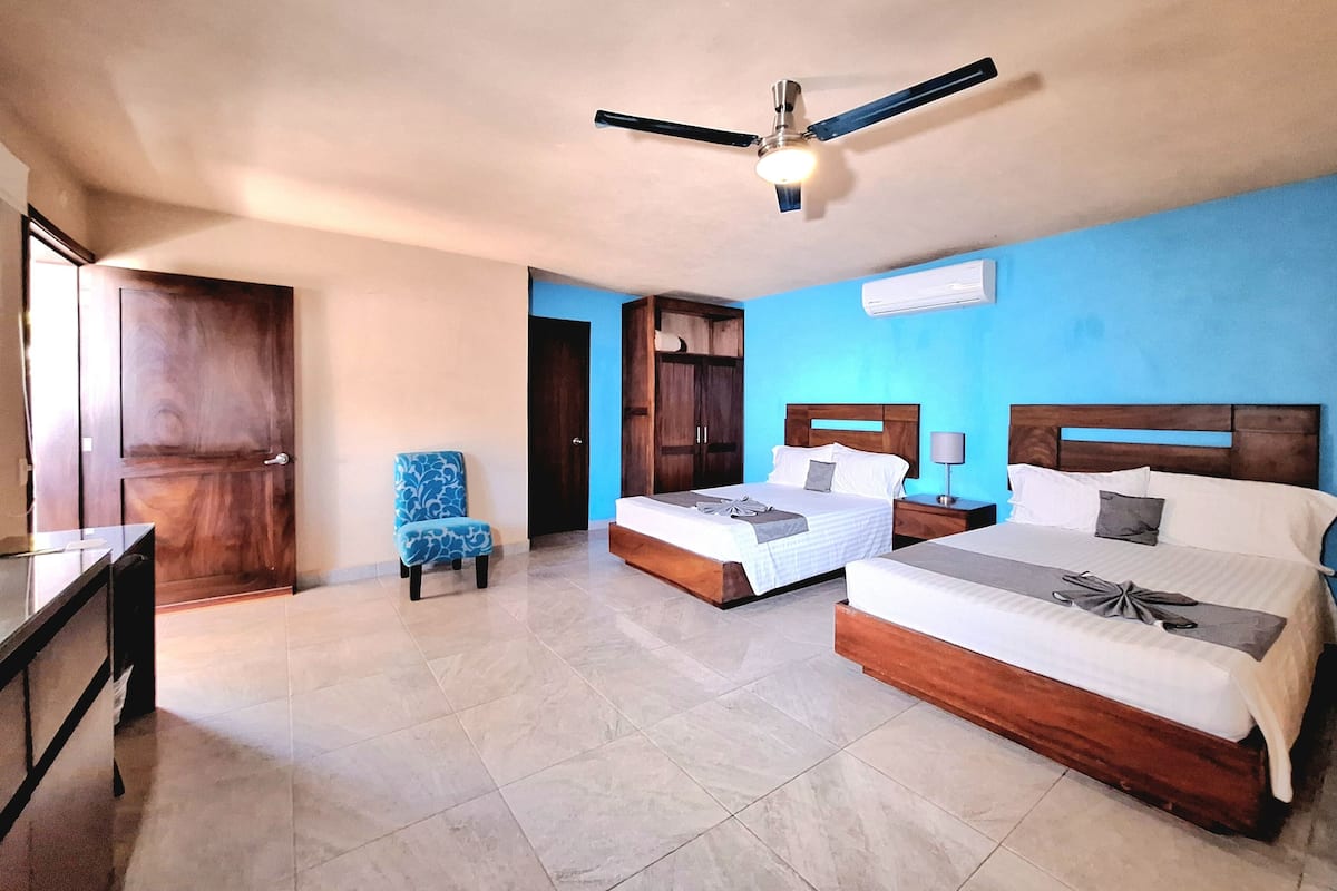 A hotel room with two beds, a desk, a chair, and a ceiling fan.