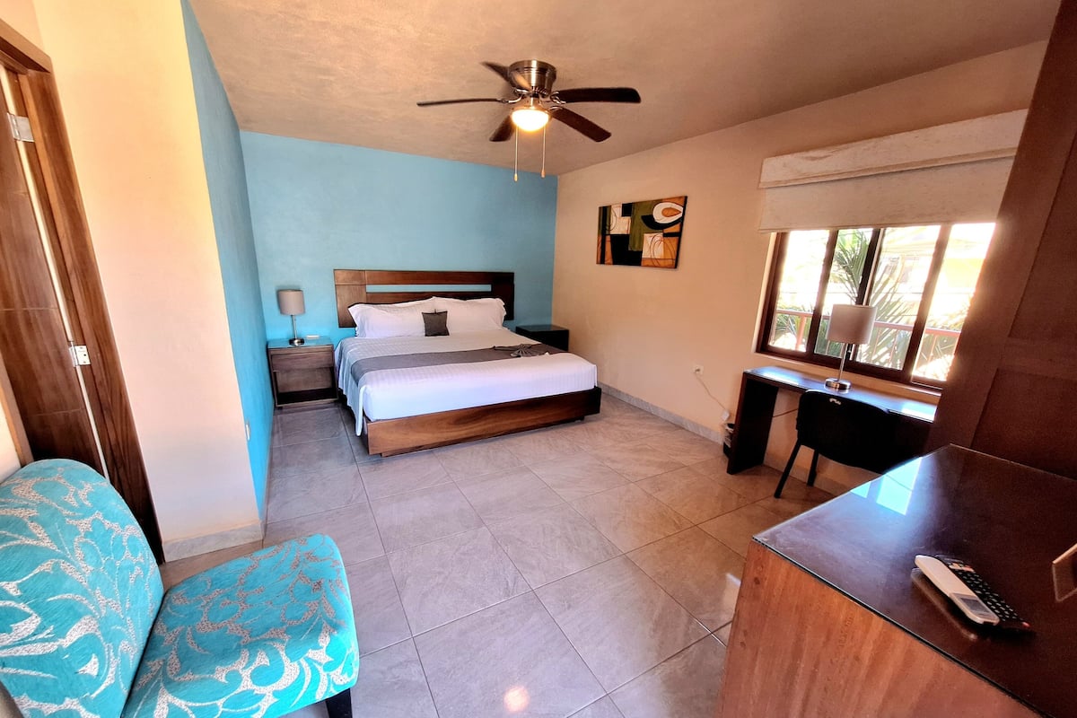 A bedroom with a bed, a desk, a chair, and a ceiling fan.