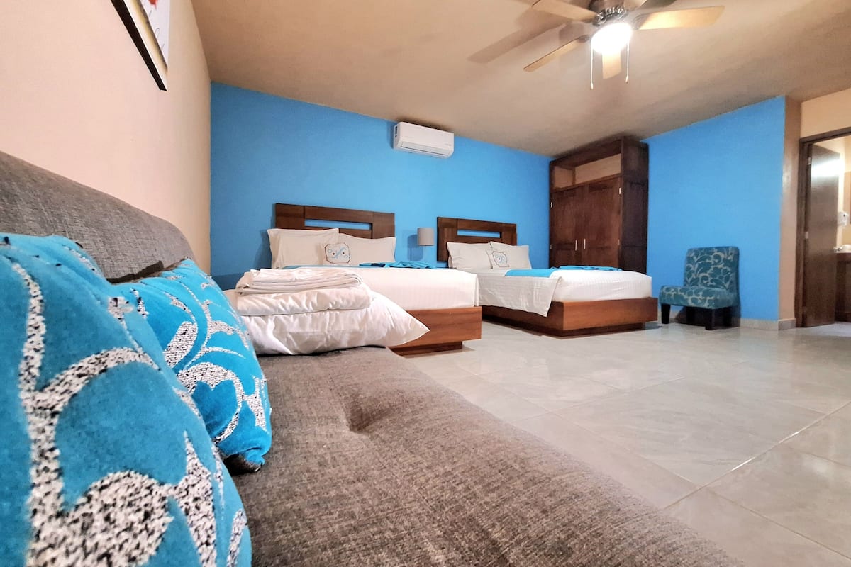 A hotel room with two beds, a ceiling fan, and a blue wall.