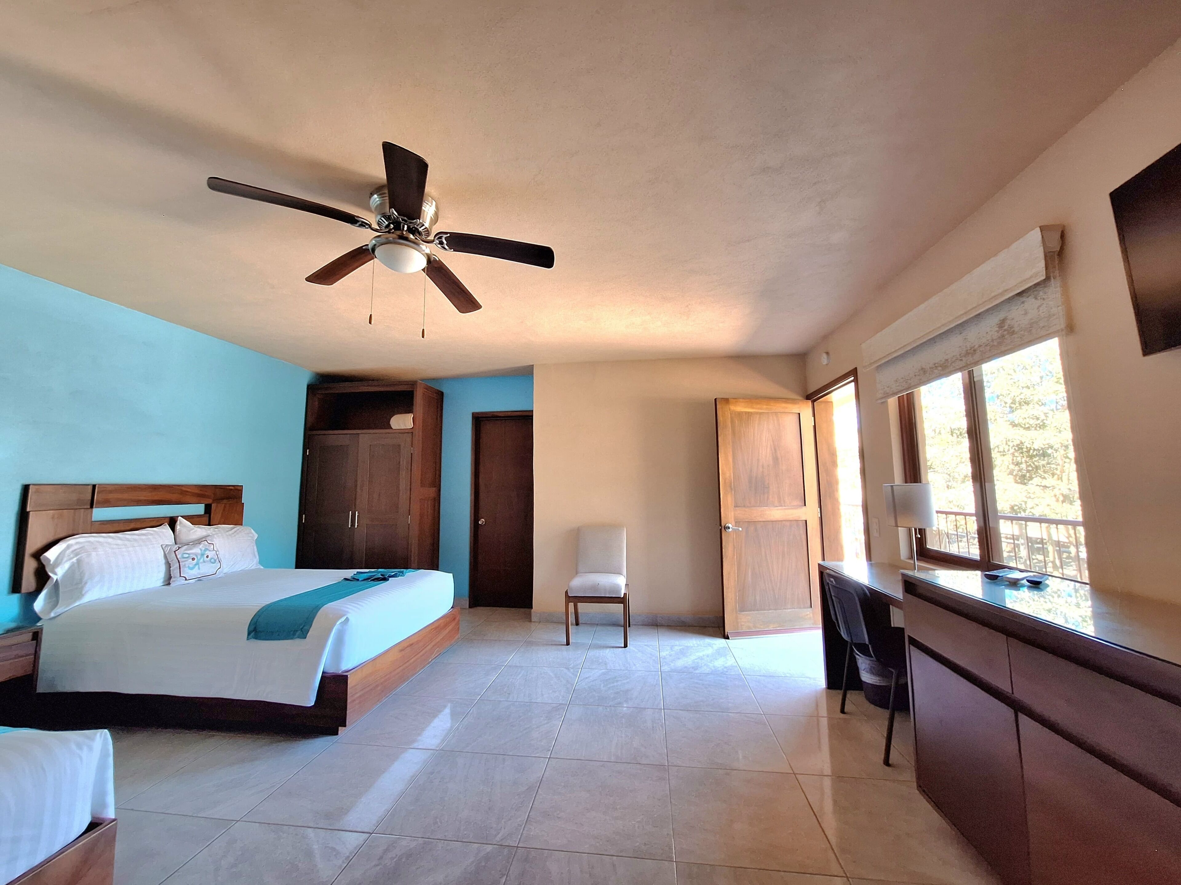Un dormitorio con cama, escritorio, silla, armario y ventilador de techo.